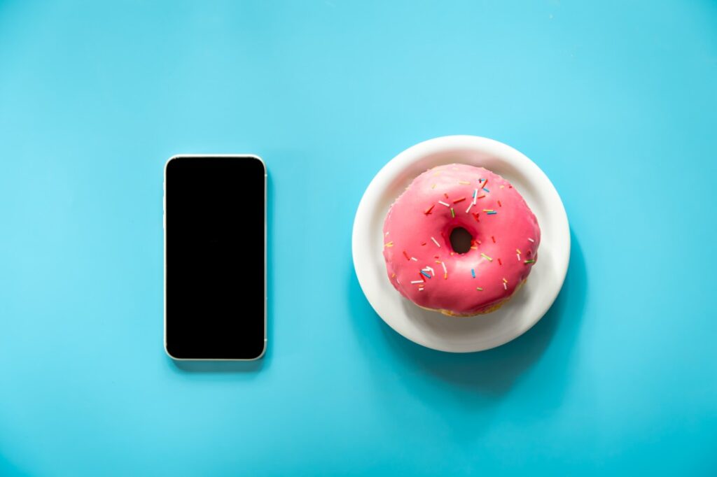 Donut with pink icing and a smartphone on a blue background