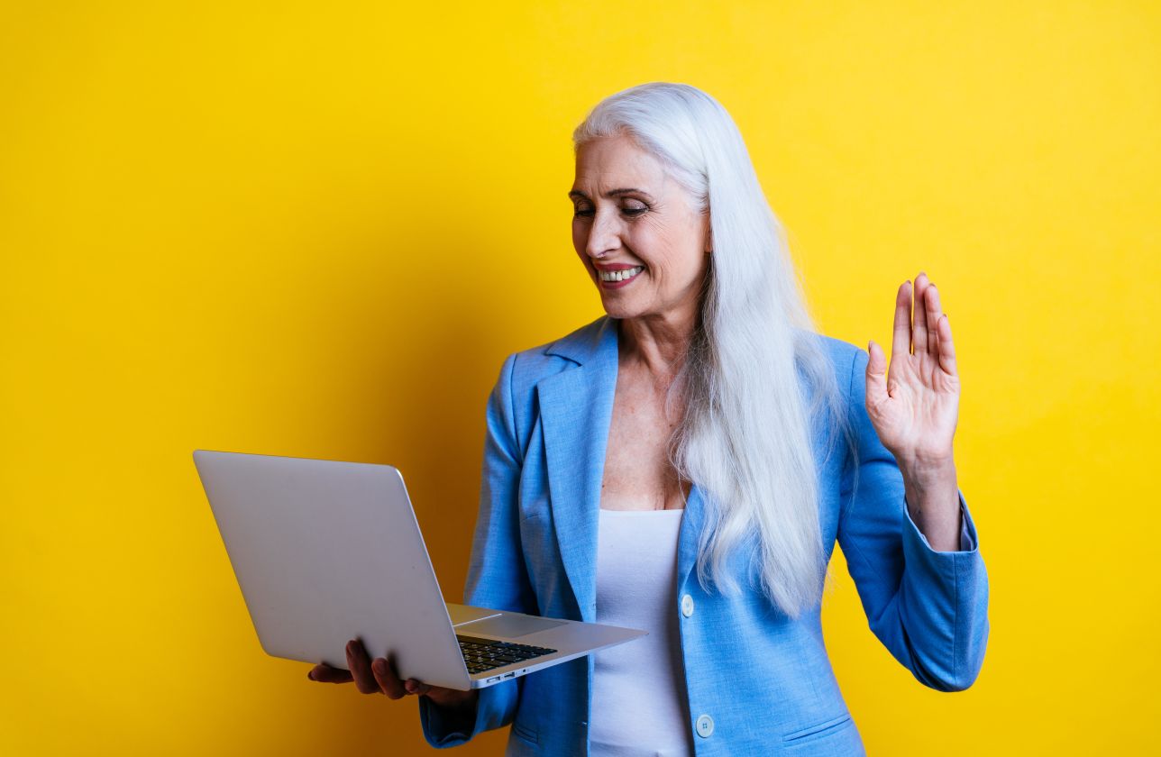 Woman talking to someone over her laptop while standing in front of a yellow background