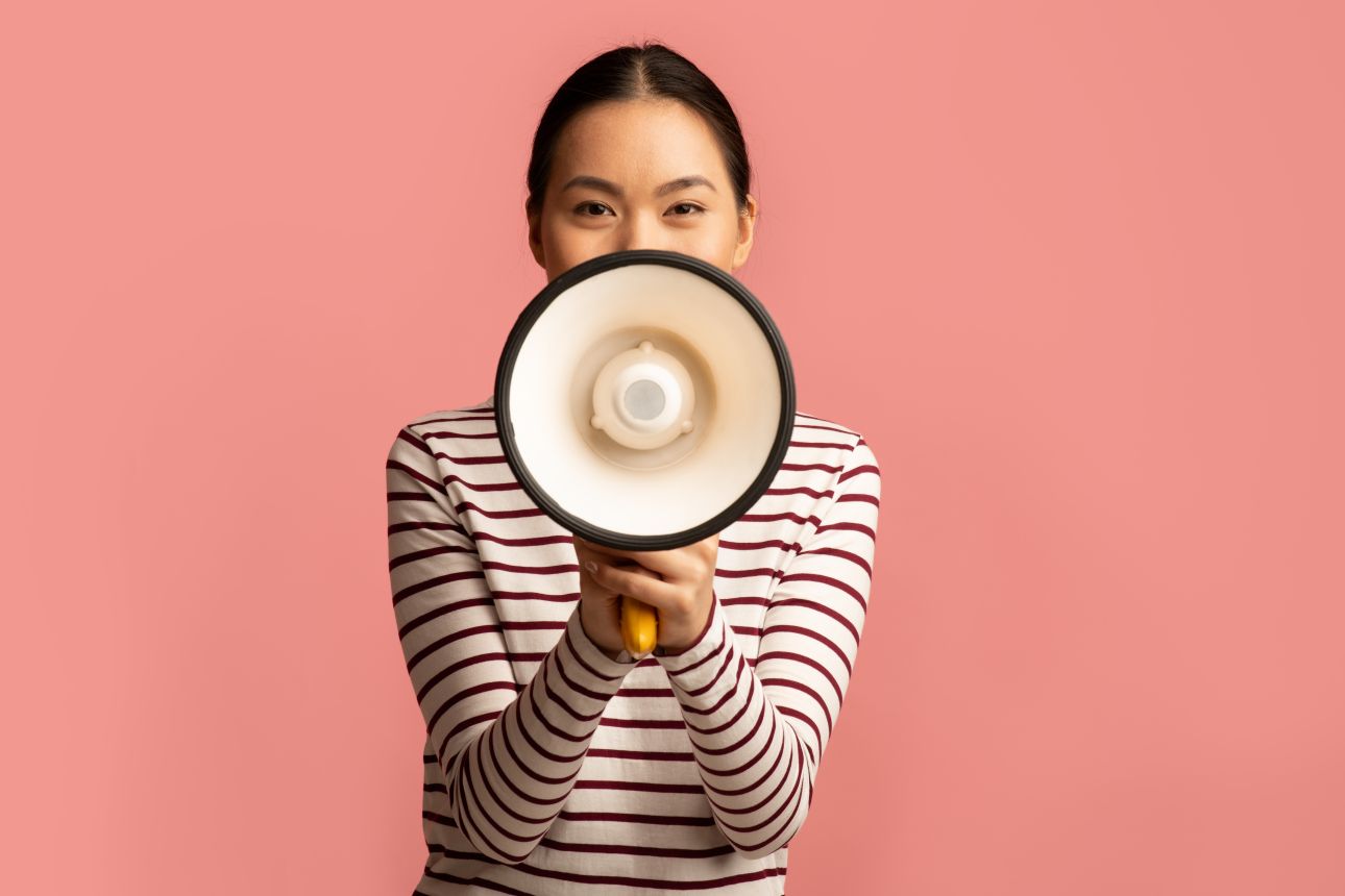 Portrait Of Young Asian Woman With Megaphone In Hands Making Announcement