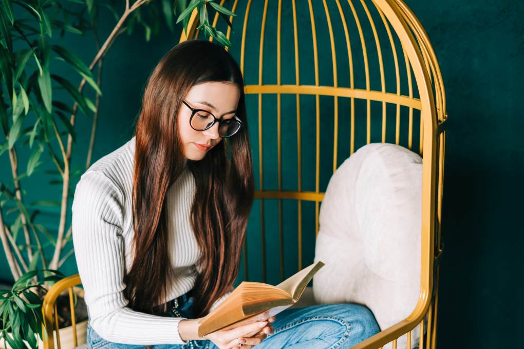 Young woman in eyeglasses sitting on sofa reading a book on creative copywriting
