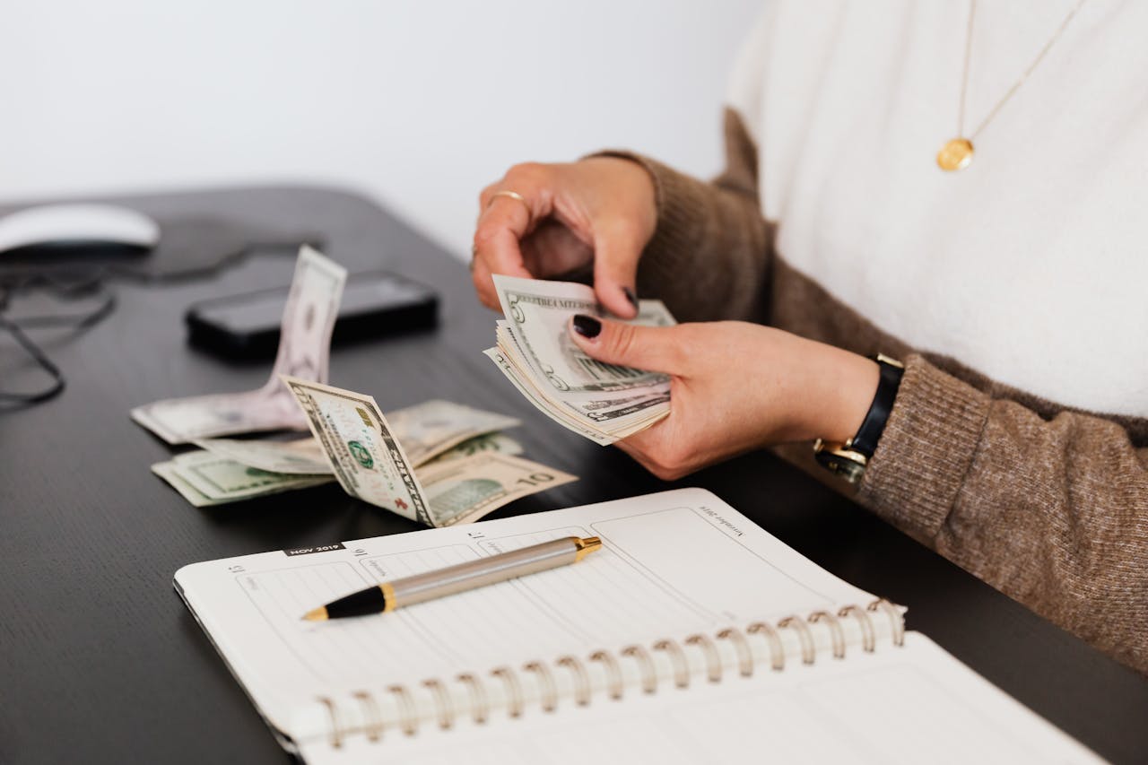 Person counting cash near a notebook and pen on a desk