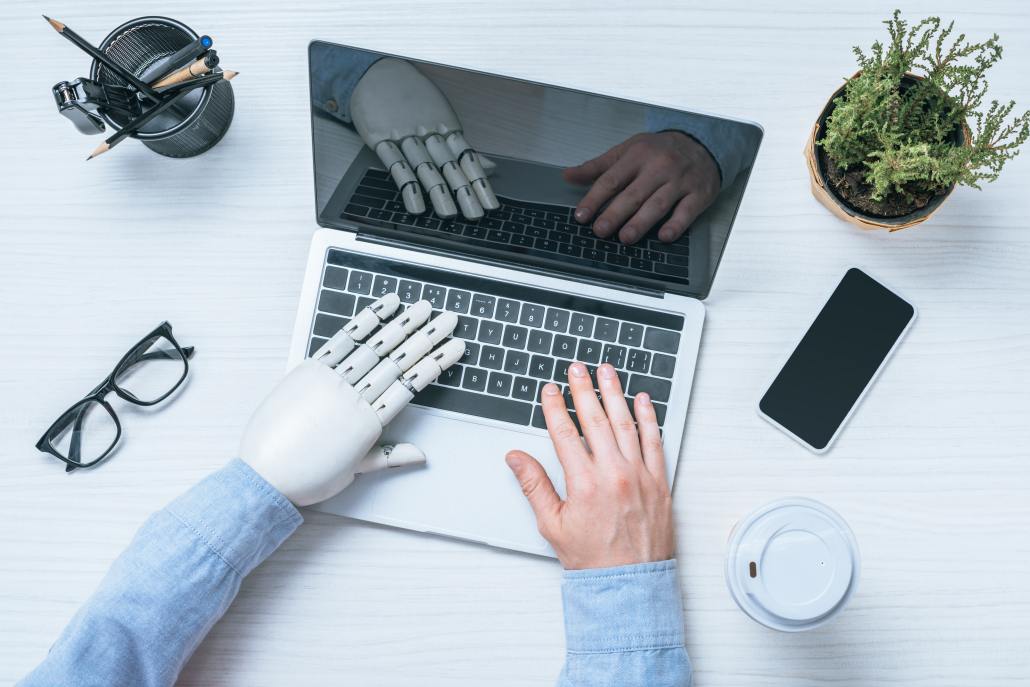 Hands of a human and a robot on a laptop doing productive work