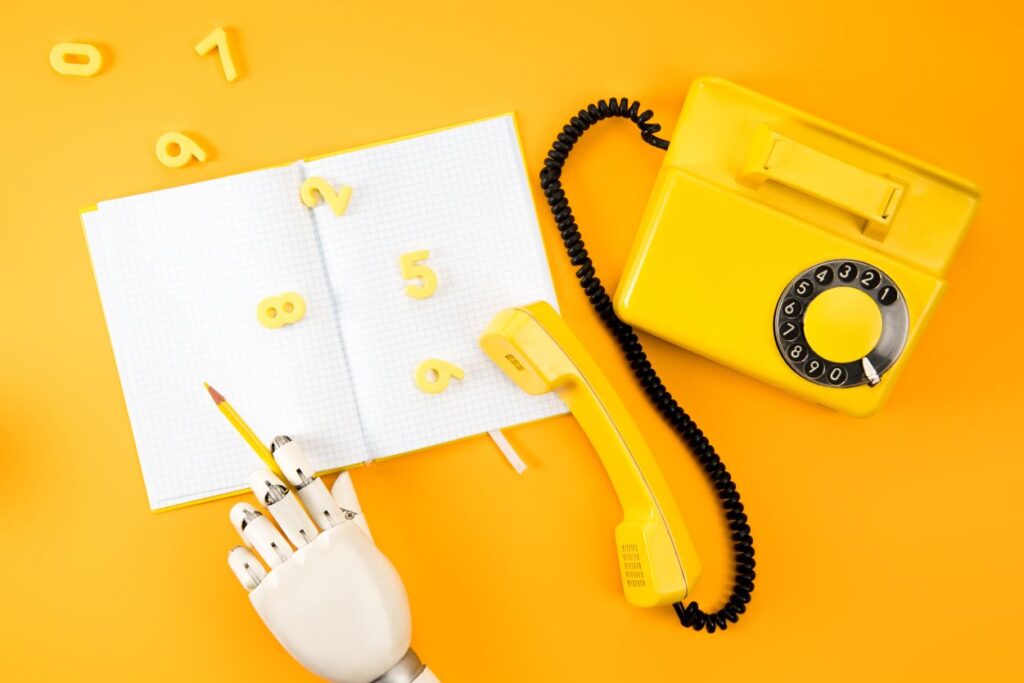 Robotic hand writing in blank notebook on yellow tabletop with vintage phone