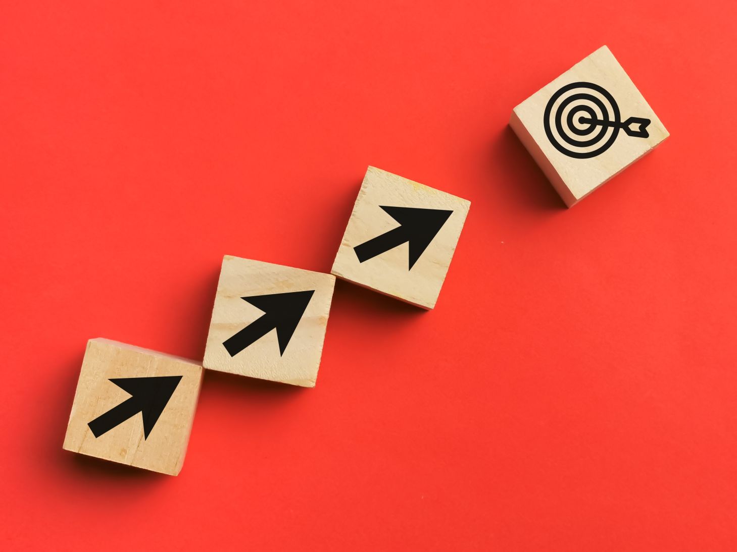 A bunch of wooden cubes line upward with arrow and dart target depicting customer journey