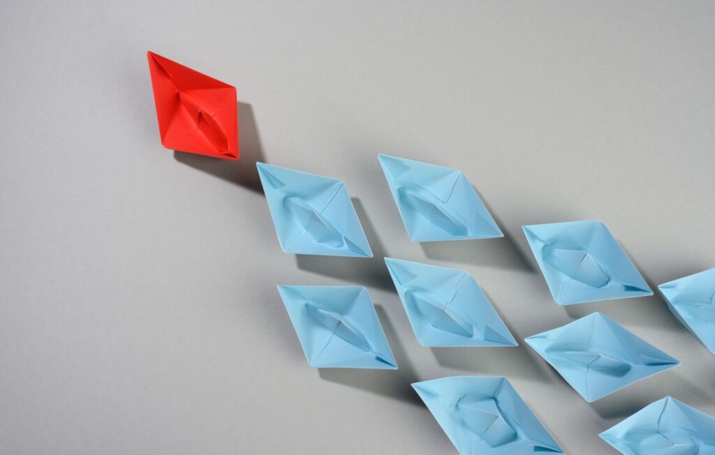 Group of paper boats on a gray background. Leadership is one of the qualities of motivational speakers