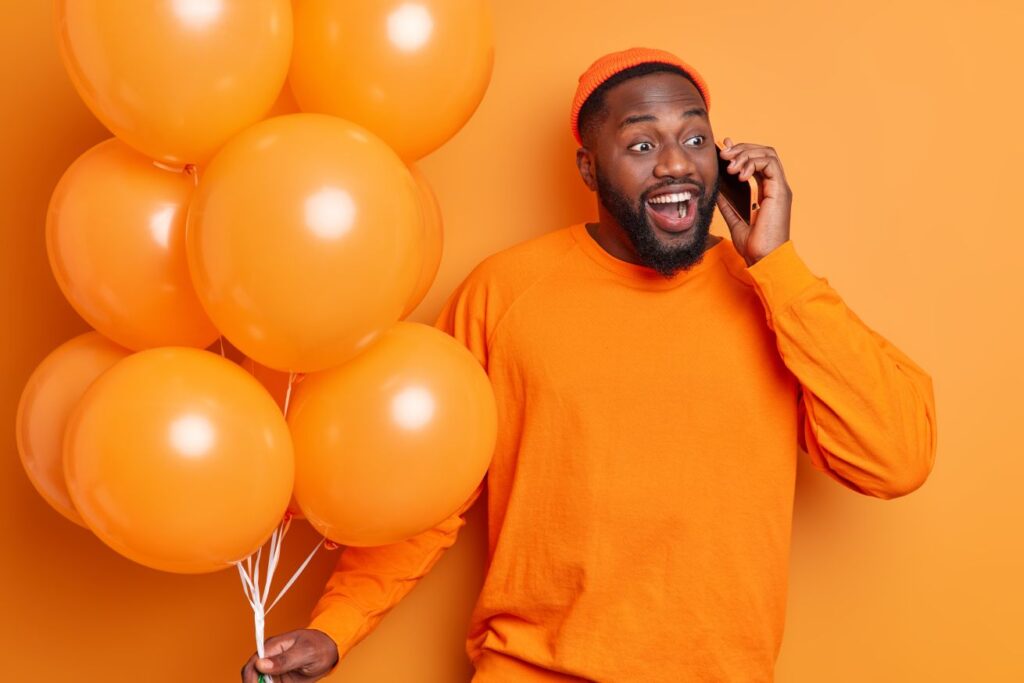 Man having a telephone conversation and smiles broadly while holding a bunch of balloons